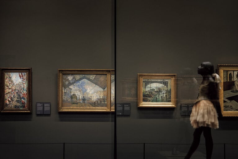 印象派展示室。中央左はモネの《サン=ラザール駅》（1877年）。左は《パリ、モントルグイユ街、1878年6月30日の祝日》。右の彫像作品はドガの《踊り子》。