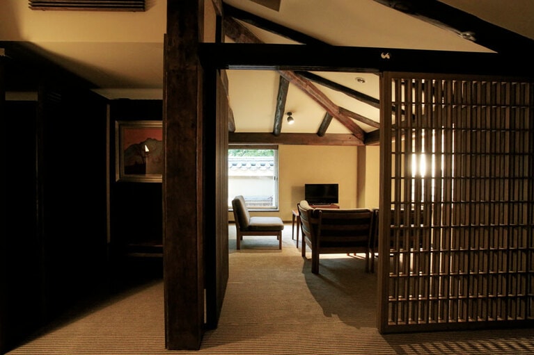 【亀の井別荘】太い梁のある天井が山荘の風情を漂わせる、本館の洋室「奥由布」のリビングと寝室。Photo: Hiroshi Mizusaki