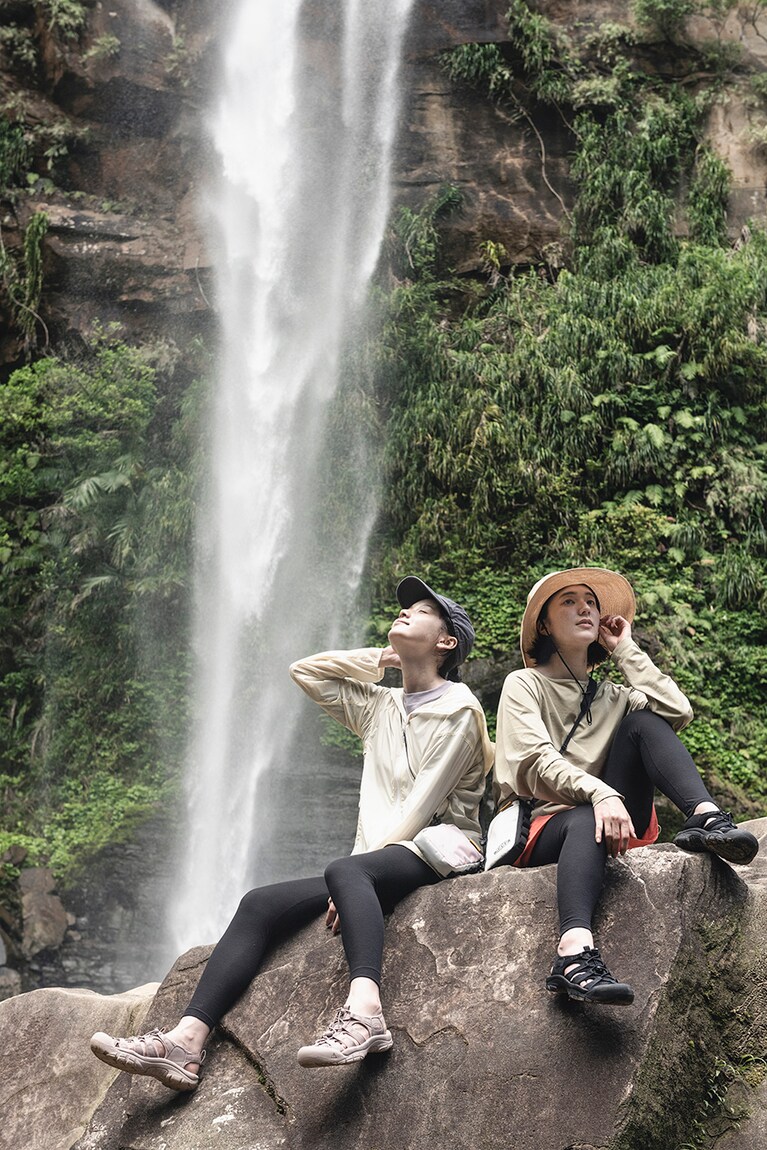 滝壺に飛び込んだり、大きな岩に登って腰掛けて滝を眺めたいというアクティブな動きも、ニューポートH2がシーンレスにサポート。モデル右：水陸両用サンダル［ニューポート エイチツー サンダル Triple Black］15,400円、サコッシュ［ハーベスト マテリアル モジュラー トラベル ポーチ White/Black］3,520円／ともにキーン(キーン・ジャパン)、Tシャツ9,900円、パンツ8,800円、帽子6,600円／以上すべてヘリーハンセン（ヘリーハンセン 原宿店　TEL 03-6418-9669）、その他／スタイリスト私物　　左：水陸両用サンダル［ニューポート エイチツー サンダル Monochrome/Fawn］15,400円、サコッシュ［ハーベスト マテリアル モジュラー トラベル ポーチ Fawn/Birch］3,520円／ともにキーン(キーン・ジャパン)、ジャケット12,980円、パンツ6,380円／ともにマーモット（サードシップ）、その他／スタイリスト私物。