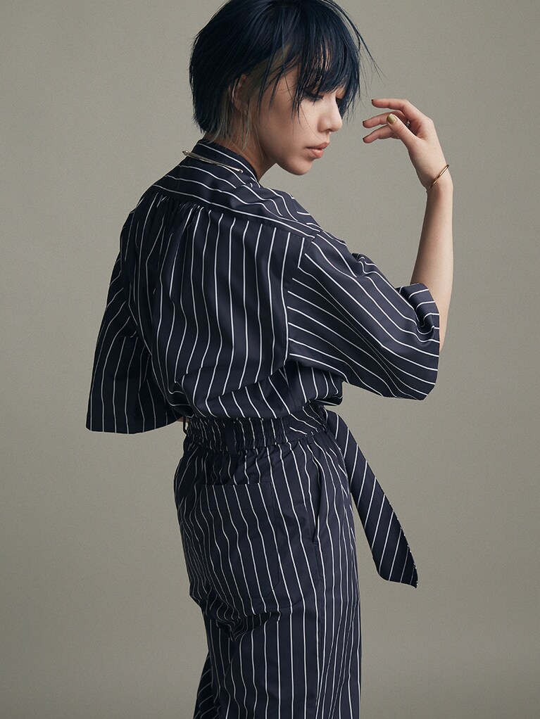 ストライプシャツ 35,200円、ストライプパンツ 42,900円/ハイク(ボウルズ 03-3719-1239)  シルバークォーターネックレス 158,400円、右腕にしたゴールドバングル 45,100円、左腕にしたシルバーチェーンブレスレット 41,800円、右手薬指にしたシルバーリング 30,800円/オール ブルース(エドストローム オフィス 03-6427-5901)  右手中指にしたシルバーリング 18,700円、左手中指にしたシルバーリング 17,600円/ミラ(スタジオ ファブワーク 03-6438-9575)  アンクルストラップパンプス/スタイリスト私物