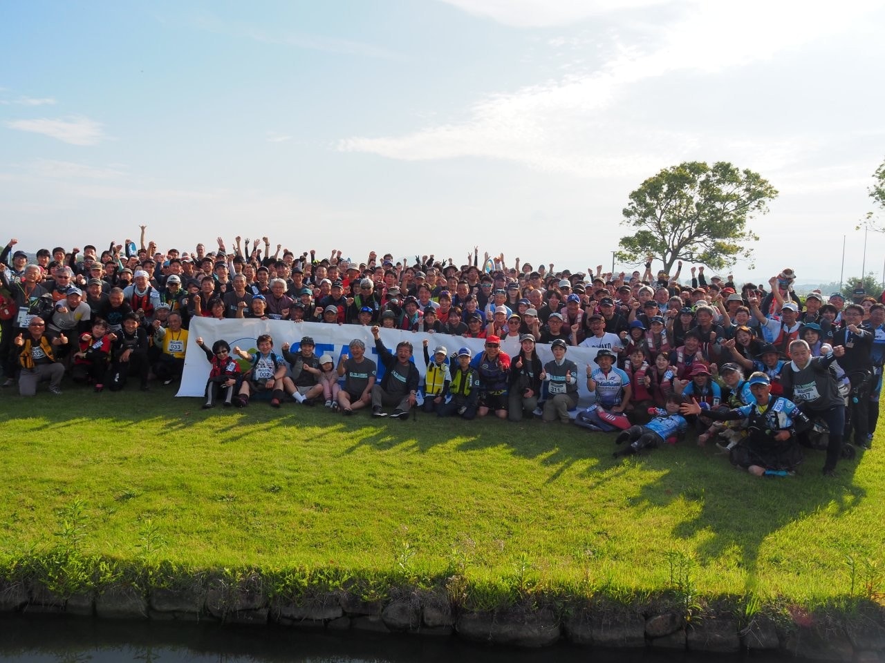 「びわ湖 東近江 SEA TO SUMMIT® 2025」の集合写真。横断幕の手前、左から5人目が、モンベル会長の辰野勇さん。(提供写真)