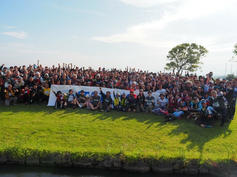 「びわ湖 東近江 SEA TO SUMMIT® 2025」の集合写真。横断幕の手前、左から5人目が、モンベル会長の辰野勇さん。（提供写真）