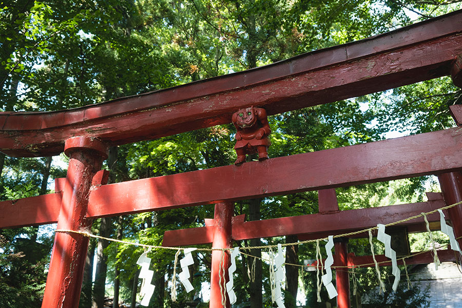 鳥居に鎮座する鬼コ。目はエメラルドグリーン、微笑みを湛えている。