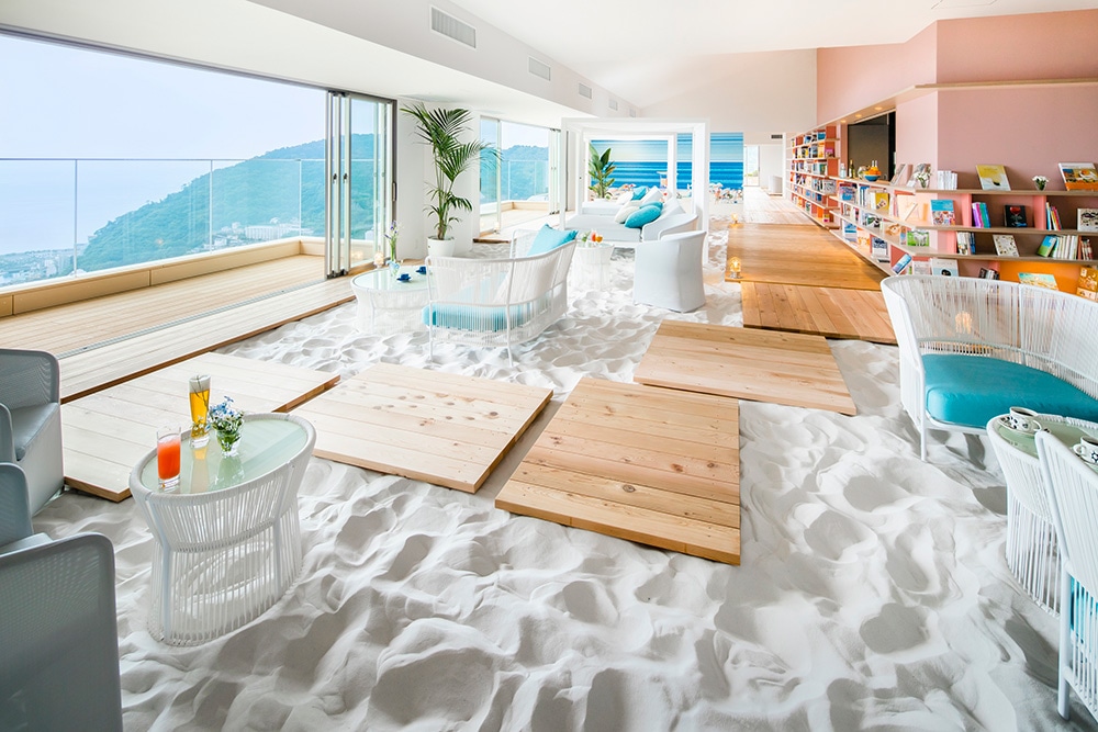 熱海の⾼台に位置するホテルの最上階という⽴地特性を活かした快適空間。喧騒から離れ、⼤⼈がくつろげる落ち着いた雰囲気のビーチを表現した「ソラノビーチ Books & Café」。