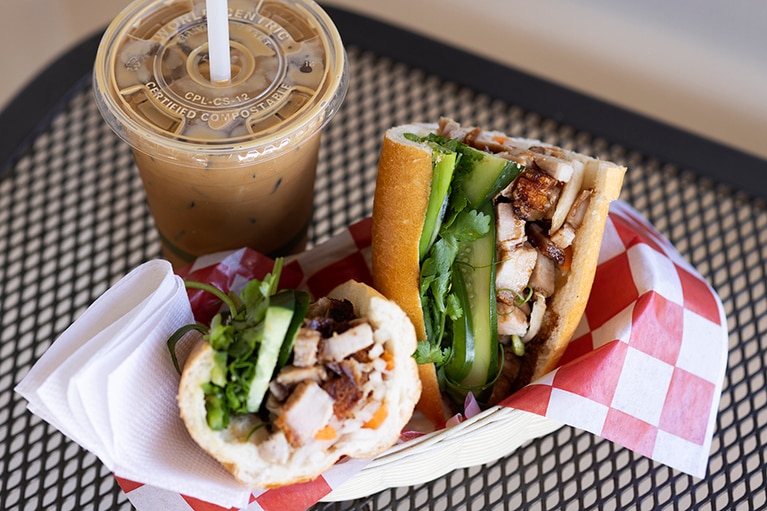 パクチーの風味とキュウリの食感がアクセントを効かせる“ローストポークのバインミー” 10.5ドル。本国同様の道具を使って淹れた“ベトナミーズアイスコーヒー” 5ドル。