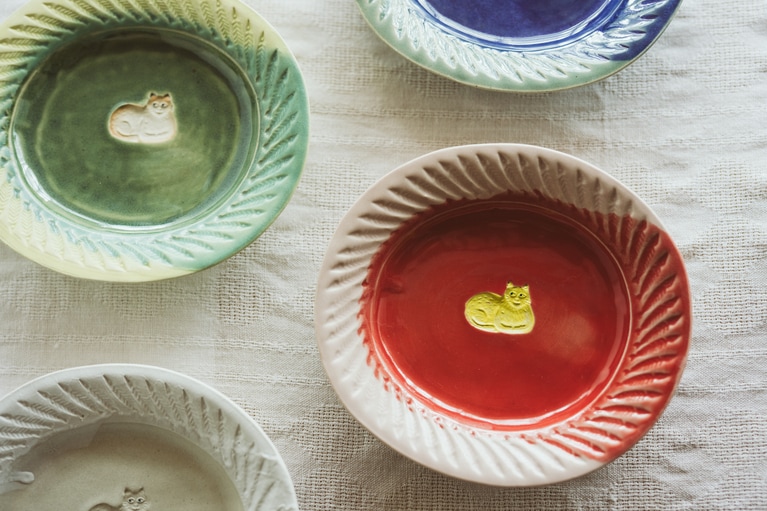 香箱座りの猫がポイントの「掛け分け印花皿」各6,600円。縁を取り囲むのは……魚！