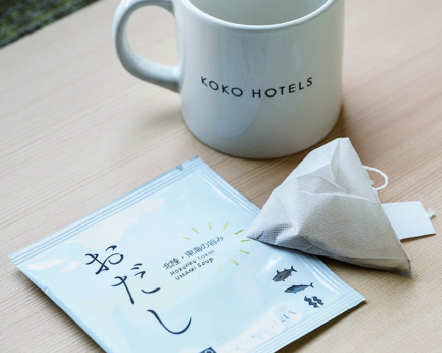 【うれしい「お出汁パック」サービス】フロントで手渡されるオリジナルの「お出汁パック」。KOKO HOTELSならではのこのおもてなしには、“ここから見つける旅を。” をコンセプトとするホテルの想いが凝縮。金沢香林坊では昆布ベースの出汁を提供し、鰹節ベースなど、地域によって異なる5つの味を用意しています。