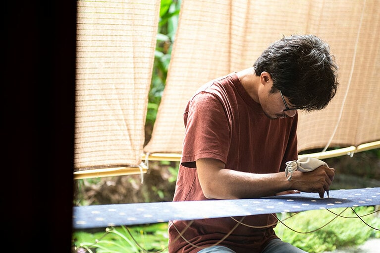 風がそよぐ工房の軒先で作業する職人さん。