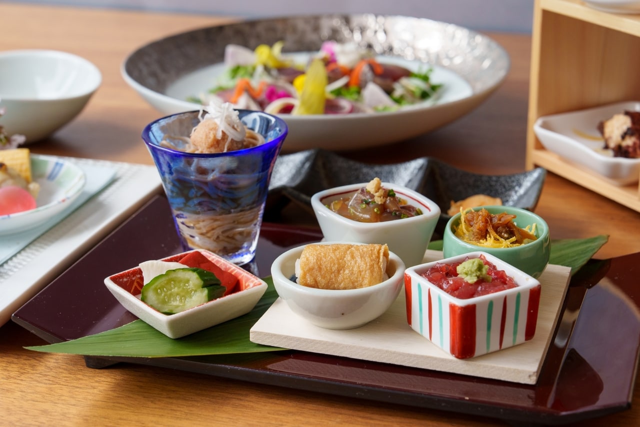 写真は2026年4月のメニュー例。5月は「山東菜の煮浸し」「牛筋と新じゃがの旨煮」「蜆の茶碗蒸し・青海苔餡」などのおばんさい5品、メイン「蛍烏賊と貝のサラダ燻製仕立て」、食事「かなっぺ寿司」「桜海老のカッペリーニ」の2品が登場予定。