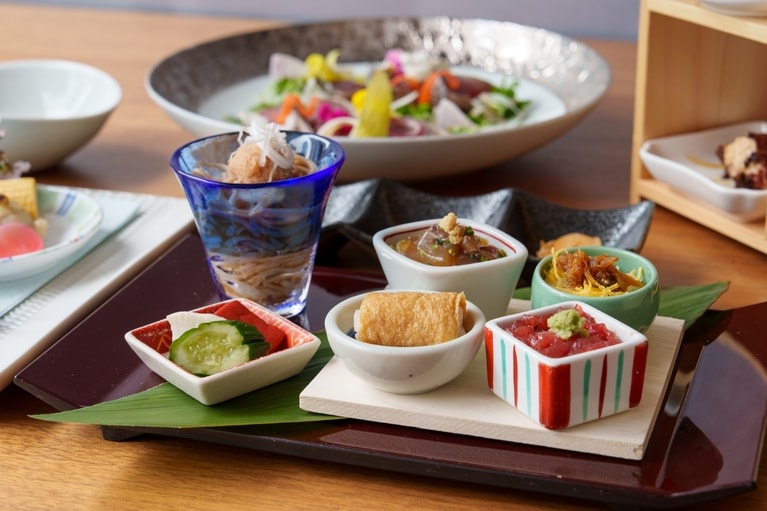 写真は2026年4月のメニュー例。5月は「山東菜の煮浸し」「牛筋と新じゃがの旨煮」「蜆の茶碗蒸し・青海苔餡」などのおばんさい5品、メイン「蛍烏賊と貝のサラダ燻製仕立て」、食事「かなっぺ寿司」「桜海老のカッペリーニ」の2品が登場予定。