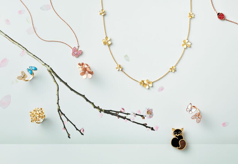 中央上から時計回り：メゾンに1920年代から引き継がれる伝統的なミラーポリッシュの技法で仕上げられたまばゆい花々。ネックレス「フリヴォル」9フラワー（YG、ダイヤモンド）2,389,200円　パピヨンは、創業時から大切に継承されるモチーフの一つ。リング「ドゥ パピヨン」アントレ レ ドア（RG、MOP、ダイヤモンド）3,286,800円　おすましキャットの愛らしい佇まいに、動物たちへ向けられるメゾンの慈愛があふれ出る。クリップ「ラッキー アニマルズ」キャット（YG、オニキス、オブシディアン）1,029,600円　光の彫刻のごとく煌めくブーケ。巧みにセットされた8つの花が、生命の喜びを表現する。リング「フリヴォル」8フラワー（YG、ダイヤモンド）1,610,400円　愛をささやきあうかのように向かいあった2匹の蝶を、指先に止まらせて。リング「ドゥ パピヨン」アントレ レ ドア（YG、ターコイズ、ダイヤモンド）3,735,600円　斜めに配したモチーフが、ひらひらと飛び回る蝶の一瞬の動きを描き出す。ペンダント「ドゥ パピヨン」（RG、ピンクサファイア、ダイヤモンド）1,966,800円　ローズゴールドの甘やかな色調に、ダイヤモンドの花芯がさらなる輝きを注ぐ。リング「フリヴォル」アントレ レ ドア（RG、ダイヤモンド）1,003,200円／すべてヴァン クリーフ＆アーペル（ヴァン クリーフ＆アーペル ル デスク）