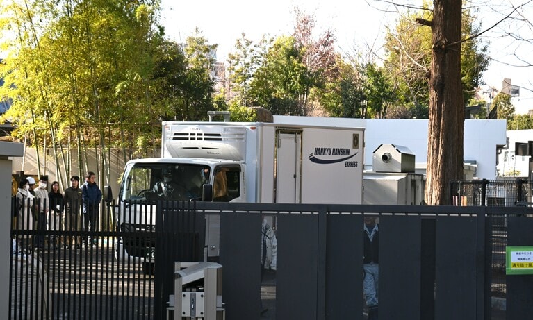 職員（写真左）に見送られながら、双子は生まれ育った「パンダのもり」を出ていった。扉には「検疫中につき 関係者以外 通り抜け禁止」とある。（2026年1月27日、園内の報道関係者用のエリアから筆者撮影）