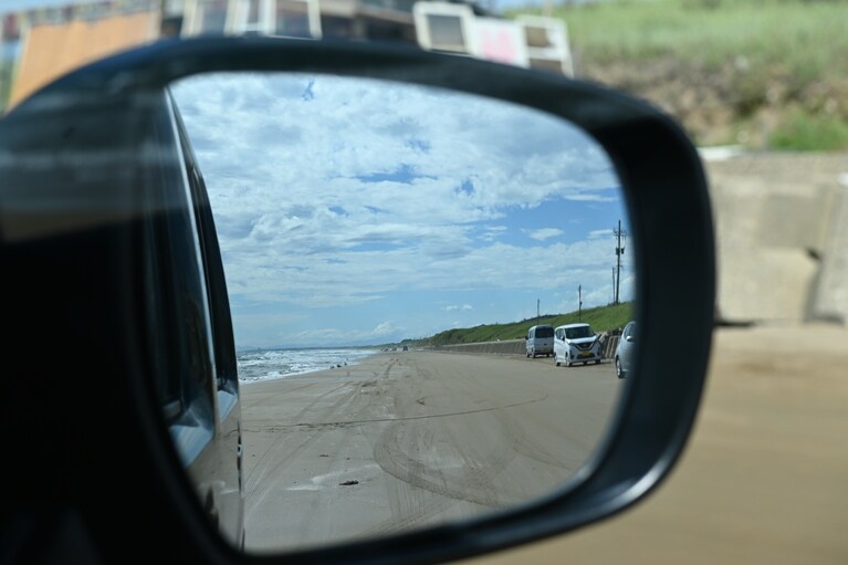 サイドミラーに映るのは、車列ではなく、渚の景色。