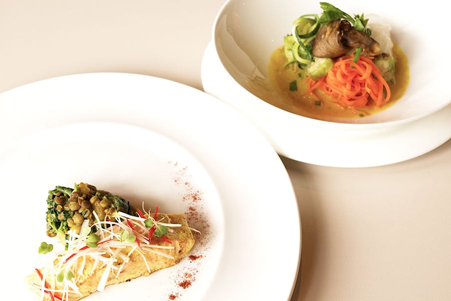 写真奥は、タイ北部の麺料理「カオソーイ」に見立てた野菜の細切りカレースープ(140キロカロリー)。手前は、タンドリーチキンにレンズ豆とほうれん草を添えた一皿(177キロカロリー)。