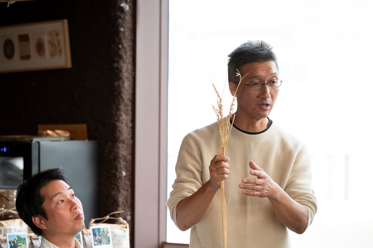 芒のついた赤米の穂を持つ、荒生勘四郎農場の荒生さん。