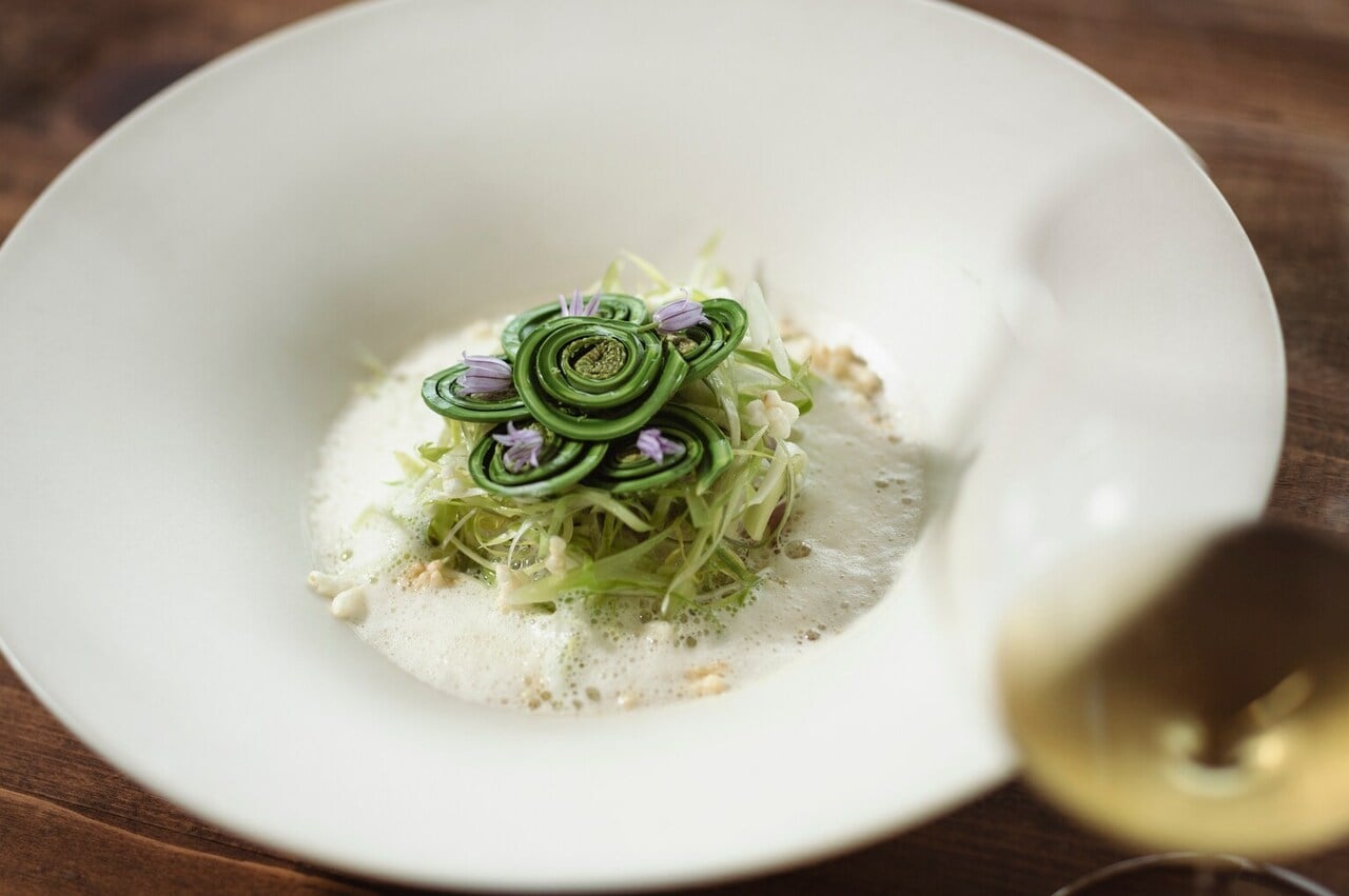 「山菜と真鯛のヴァプール」。くるくる巻かれたコゴミやアサツキの花の紫色が目を引き、その下には細く刻んだウルイがたっぷり。