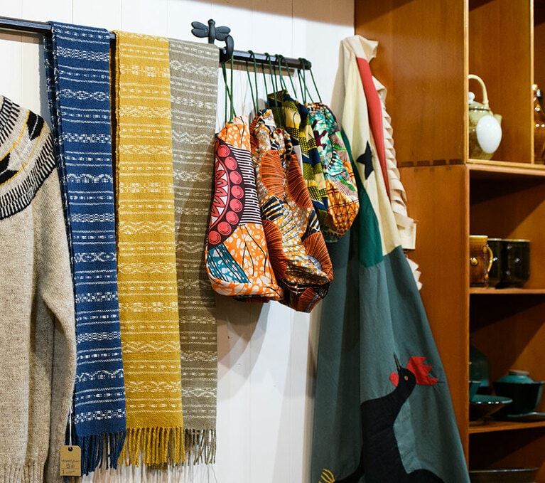 右の巾着バッグは、2人が収集したアフリカの布で製作を依頼したバッグンナウンの別注品(6,050円、7,150円)。左は岩手県・盛岡で手織りで仕立てられたホームスパンマフラー。空気をたっぷり含ませてゆっくりと紡いだ糸を使っており、非常に軽く暖かい。たくさんの織り柄が載った柄見本をそのまま反映したユニークな別注もお見事(各40,000円)。