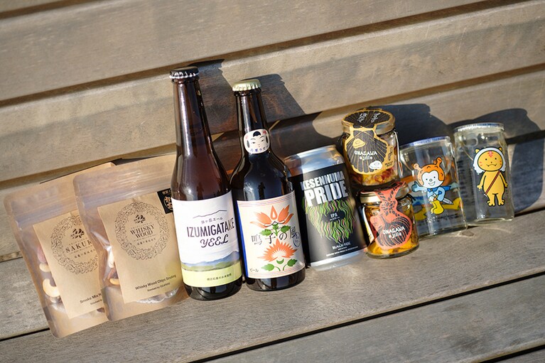 左から、塩竈の藻塩を使った「燻製工房おが太朗」の燻製ミックスナッツ450円、イシノマキファーム「泉ヶ岳エール」（現在は「巻風エール」700円を発売中）、鳴子温泉ブルワリー「高原ラガー瓶」616円、クラフトビールのブラックタイドブリューイング「KESENNUMA PRIDE」（現在は店頭に無し）、三陸の海の幸を瓶詰した岡清「女川（おながわ）アヒージョ」ほたて864円、ほや972円、気仙沼の酒蔵･角星の「ホヤぼーや」385円、ゆるキャラのワンカップなど、お酒もつまみも充実。