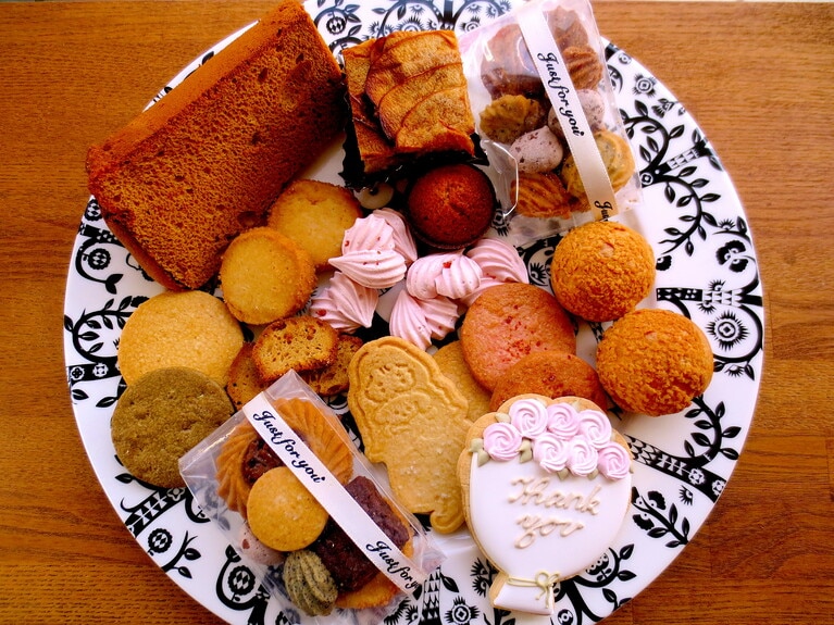 左上より時計回りに「米粉のキャラメルシフォンケーキ」290円、「りんごのケーキ」280円、「おつまみミニアソート」550円、「シュークリーム」プレーン120円、紅茶クリーム130円、「アイシングクッキー」500円、「サブレアソート」ミニ550円、「米粉のほうじ茶サブレ」1袋（2枚）200円、「塩サブレ」1枚70円・1袋（2枚）150円、「豆乳サブレ」1枚100円・1袋（2枚）210円、「発酵バターのフィナンシェ」160円、「いちごのメレンゲ」1袋330円、「いちごサブレ」1袋（2枚）200円、「DOUDOUサブレ」120円、「フィナンシェラスク」1袋380円。