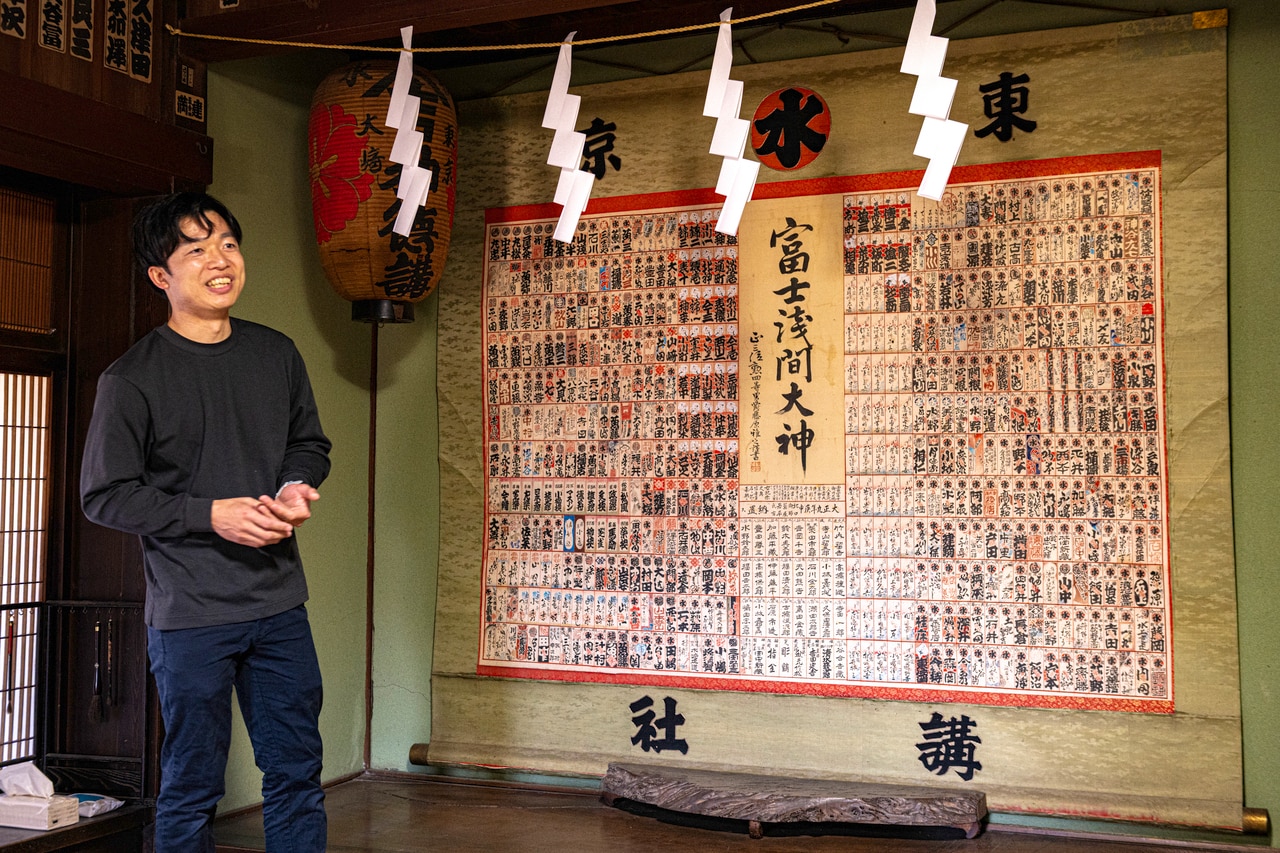 紙垂を張った床の間を案内する、菊谷坊18代当主・秋山真一氏。東京・丸水講社が大正9年に奉納した畳2畳半の掛け軸には、560名の講員名が記されている。