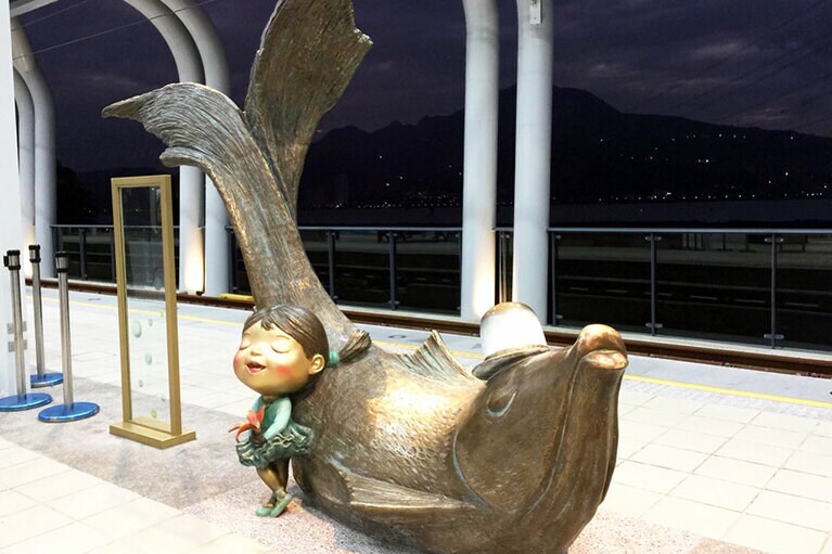 魚と子供のオブジェの背景は淡水河。