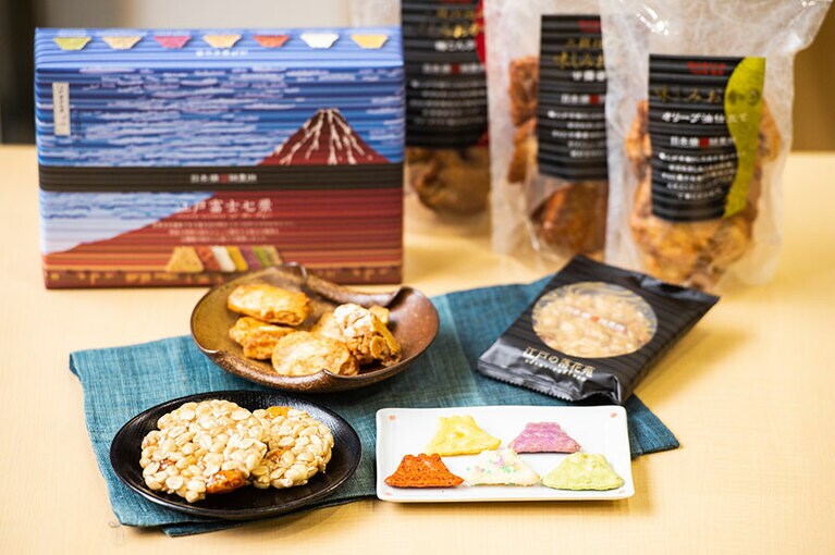 お皿・手前左から：江戸の落花苑(9枚入) 2,160円、味しみおかき3種詰合せ 120g×3種 2,592円、江戸富士七景(7種×3枚) 594円(すべて税込)。