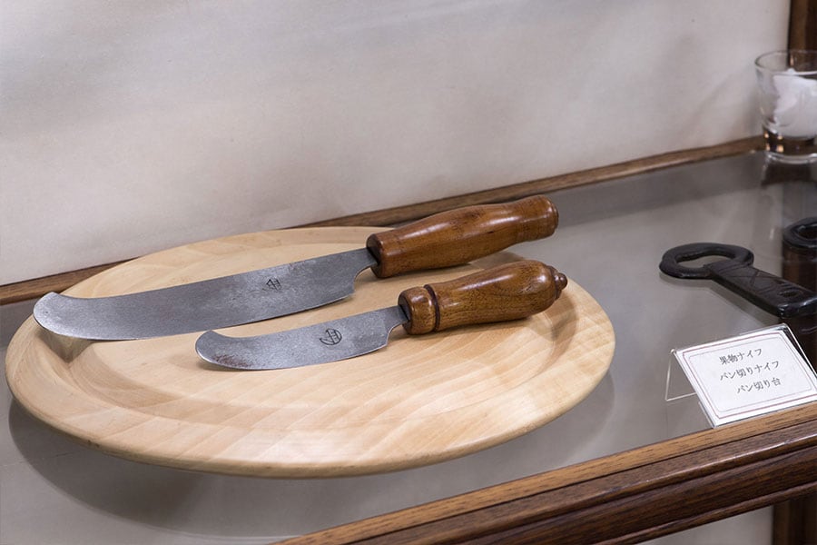 吉田璋也が考案したパン切りナイフとパン切り台、果物ナイフ。ナイフは中国の青龍刀をヒントに使いやすくアレンジしたもの。パン切り台には、屑がこぼれないように溝がついている(鳥取民藝美術館所蔵)。