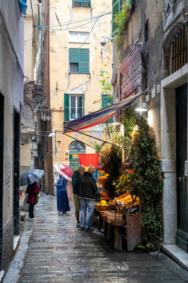 旧市街の路地に佇む八百屋。雨でしっとりと濡れた石畳が絵になる風景。