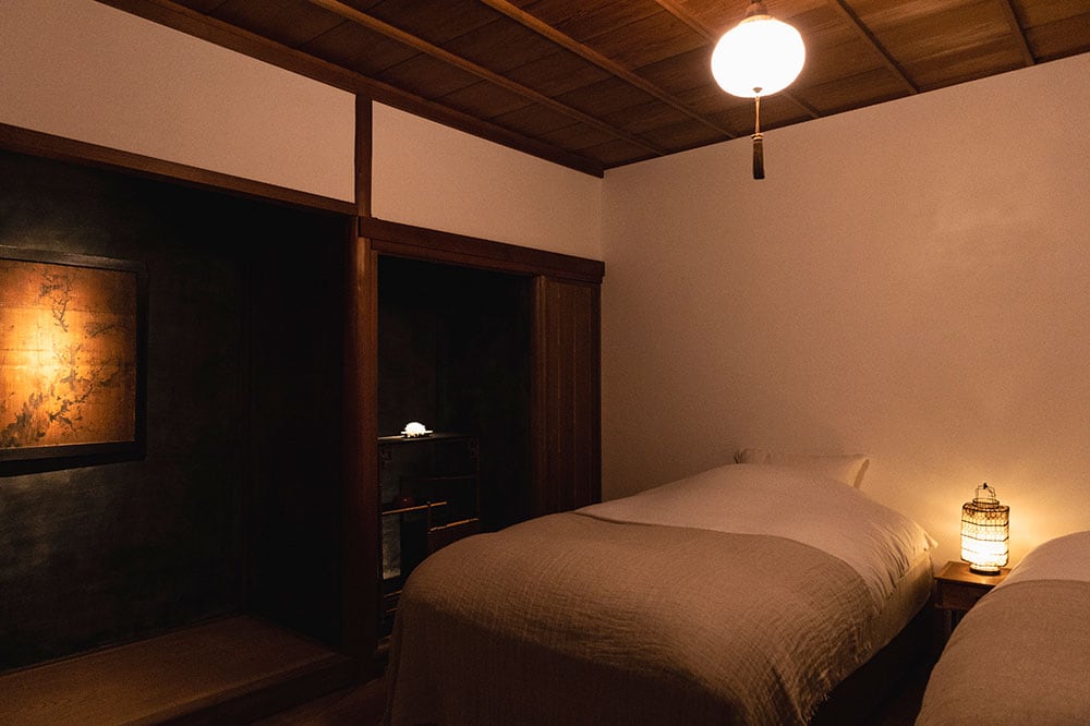 黒漆喰の床の間と白壁のコントラストが印象的な「room 1」。夜の海のような壁に、江戸時代の杉戸絵が映える。竹を100％使用した竹布のベッドリネンはしなやかで寝心地がよい。