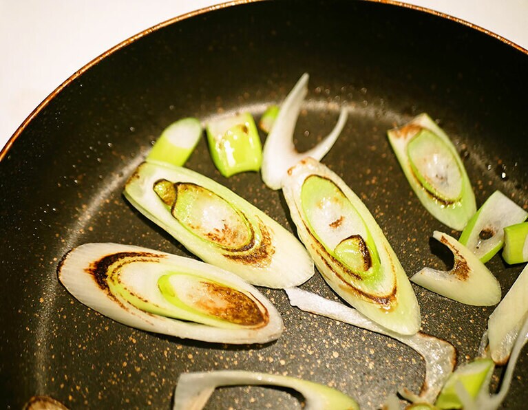 フライパンにごま油をひいて、強めの中火にかける。ショウガ、ネギを入れて、90秒ぐらいそのまま置く。ネギにしっかり焼き色がついたら返して、今度は60秒ぐらい焼く。