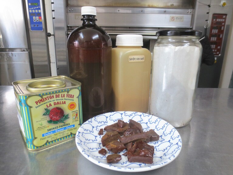 こだわりの調味料いろいろ。左からスペイン産スモークパプリカパウダー、自家製のスモーク醤油、スモーク塩、右端の瓶と前の皿は、スモークパウダー（ヒッコリースモーク）を固形にしたもの。