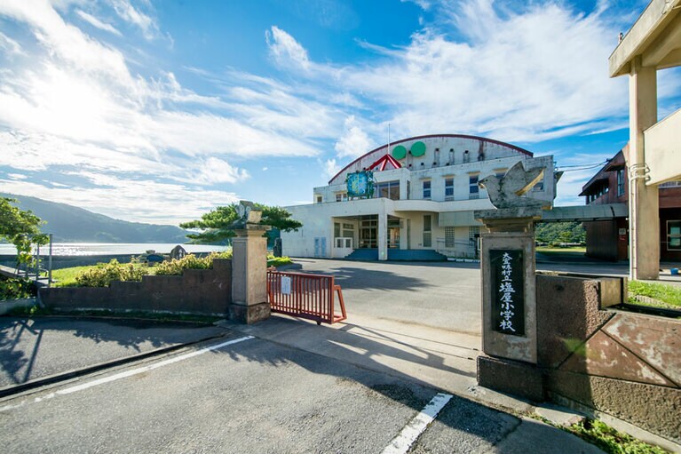 青い海に浮かんでいるハコブネのように見える赤い屋根の体育館が目印の大宜味村立旧塩屋小学校(大宜味ユーティリティーセンター)。