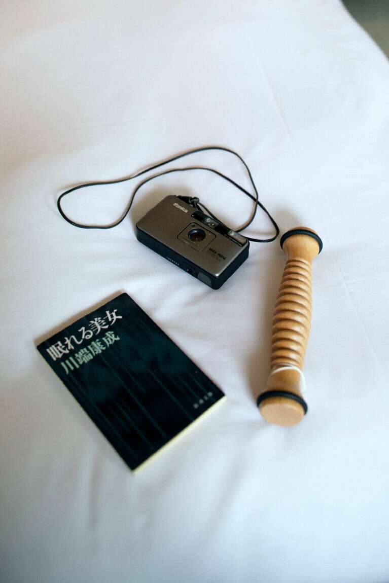 左から時計まわりに：「繰り返し読む好きな本、気になる新書、旅先で見つけた可愛い本屋さんで買った写真集など、旅先でも読書の時間を楽しみます。紙の本のページをめくるあの感覚が好きです」。　コニカ「ビッグミニ」。90年代に大流行したコンパクトミニカメラ。「旅の思い出はフィルムに記録します」 。　チャコットにて購入した足裏コロコロ。「マッサージ、むくみとりに」。(すべて飯島さん私物)