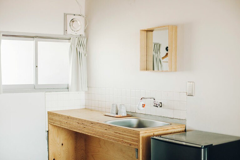 シンク、冷蔵庫、電気ケトル、テーブル＆チェア。必要最小限なものが揃う室内。