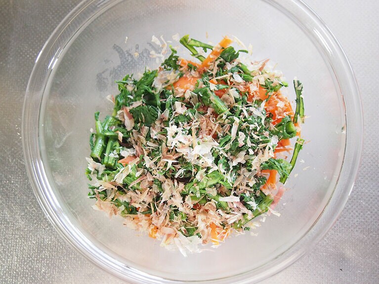 (5) 春菊は生でも食べられるので、サッと茹でる程度で大丈夫です。茹でたら冷水に取り出し、すぐに冷まします。 水分を絞ったら、4センチ長さに切り、ボウルに入れます。 (3)の人参、鰹節、醤油、黒酢を入れて混ぜます。