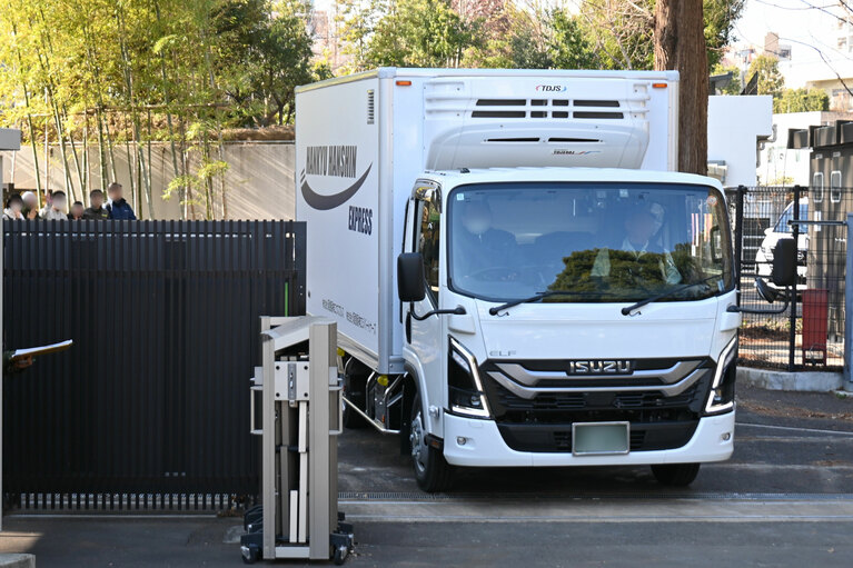 パンダの飼育施設を出る、双子をのせたトラック。手を振りながら見送る職員も。開園時間中の出発だったので、園路の一部が一時的に通行止めとなった。（2026年1月27日、園内の報道関係者用のエリアから筆者撮影）