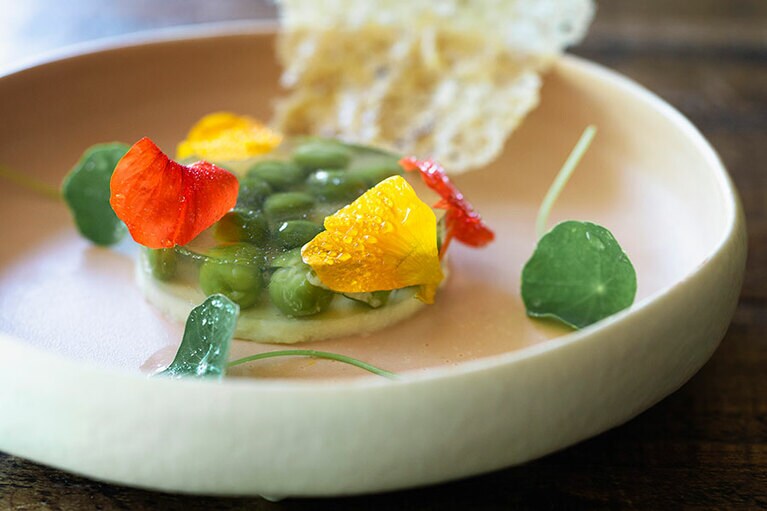 玉ネギのブランマンジェの上に、“トマトの涙”と呼ばれるエキスでエンドウ豆を閉じ込めたものをのせ、チュイルとナスタチウムを添えた“翠雨”。