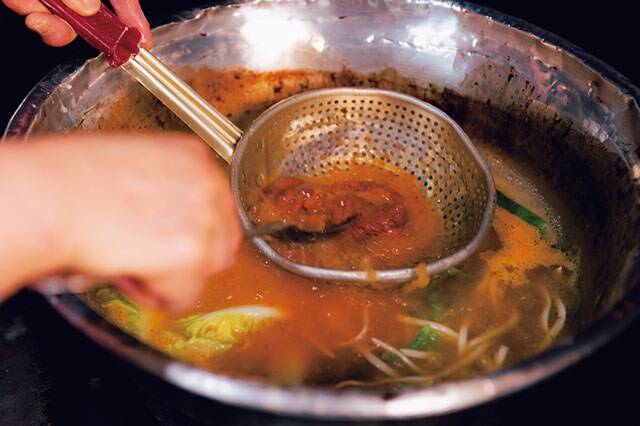 注文ごとにスープを煮立て、季節の野菜と麵を煮る。最後に穴杓子でジャンを溶き入れる。