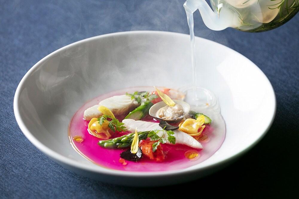 仕上げにスープをかけると皿の上で半透明だった色が赤く変わる、驚きの演出が隠された“魚介のパナッシュフュメドコキヤージュ”。