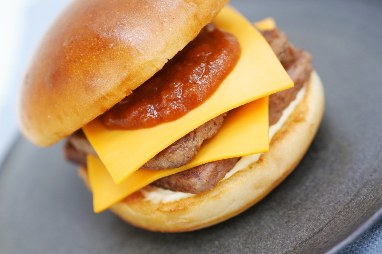 「『モスの匠味』黒毛和牛のダブルチーズバーガー」890円。パリっと触感のあるプレミアムバンズに黒毛和牛パティを2枚、チーズを2枚。オニオントマトソースはケイジャンシーズニングを加えることでややピリカラ風味に。次の一口が止まらない無限ループであっという間に完食です！