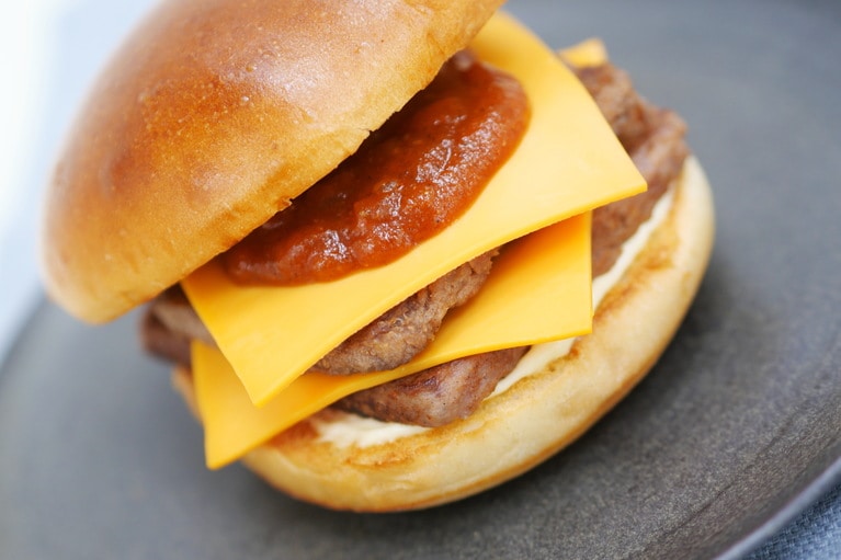 「『モスの匠味』黒毛和牛のダブルチーズバーガー」890円。パリっと触感のあるプレミアムバンズに黒毛和牛パティを2枚、チーズを2枚。オニオントマトソースはケイジャンシーズニングを加えることでややピリカラ風味に。次の一口が止まらない無限ループであっという間に完食です！