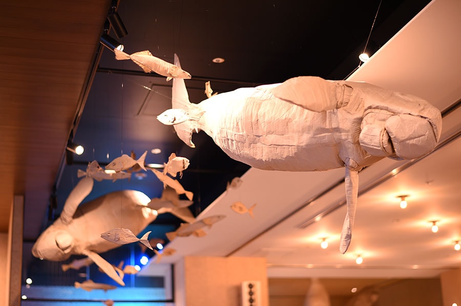 天井に飾られるのは、段ボールを用いてジュゴンなどの海洋生物をつくり、環境問題を訴えるアート作品。米国人アーティストのアンバー・ダーウェン氏によるもの。