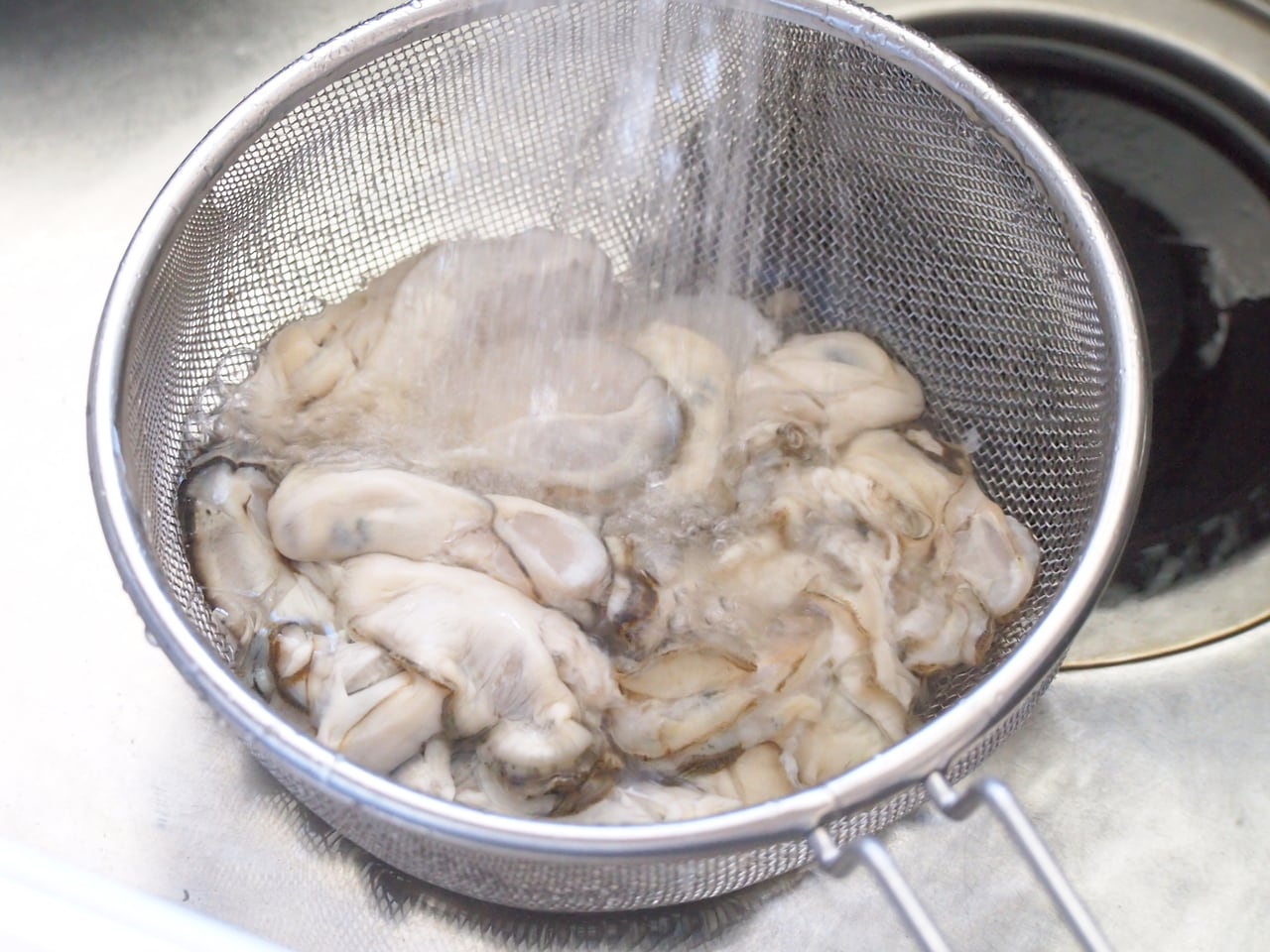 牡蠣はザルに入れ、ぐるぐると回すように水を入れながら汚れを落とす。