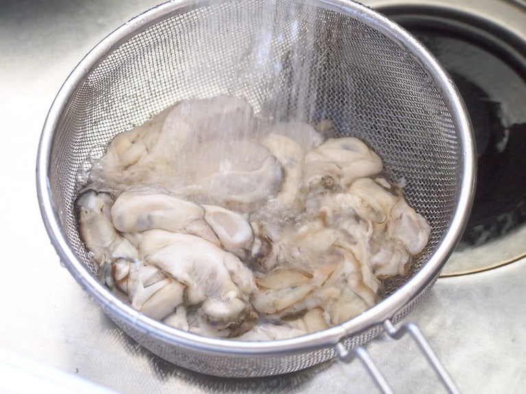 牡蠣はザルに入れ、ぐるぐると回すように水を入れながら汚れを落とす。