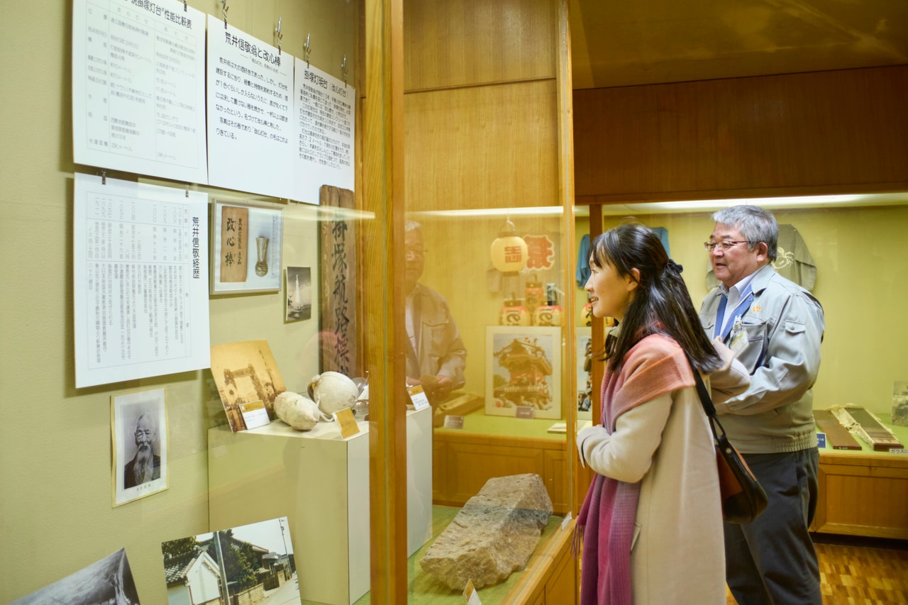 竜洋郷土資料館で、掛塚湊の繁栄の礎となる改心灯台を造った荒井信敬について佐藤さんの説明を受ける。倹約のための盃「改心棒」に、永井さんは興味津々の様子。