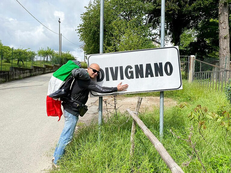 出発日、市の看板に寄り添うバケッタ市長。リュックにサンダルという軽装！