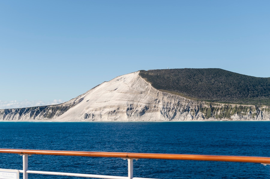 にっぽん丸はゆっくり新島を通過。火山灰の地層が露出した絶壁「白ママ断層」と青空とのコントラストは、まさに映え。