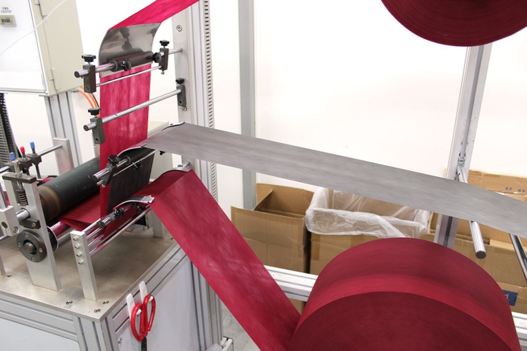 フィルターとなるメルトブロー不織布を2種類のPP不織布で挟み、三層構造にする工程。中間層の色が製品の色味の決め手。ここでは黒を選び、臙脂色に深みを出している。