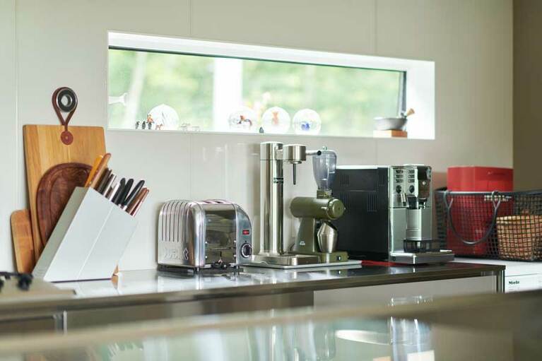 家時間が増えたことでキッチンアイテムもさらに充実。「アアルケ」のソーダサーバー、「ガジア」のエスプレッソマシン、「カリタ」のコーヒーミルなど。窓ぎわに並べたスイスのスノードームも可愛い。設計／モリノイエ(https://i-morinoie.com/)