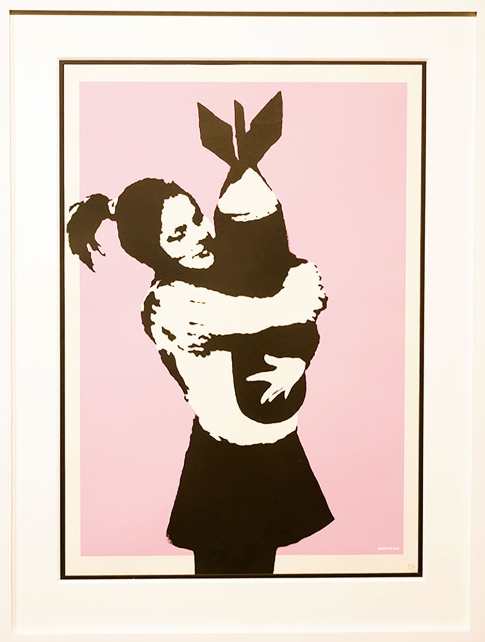 【愛】1998年、バンクシーがステンシルで描いた《ボム・ラブ》。無邪気な笑みを浮かべる少女に抱きしめられたら、その愛情によって爆弾だって無力化できるかもしれない。